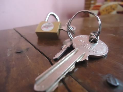 A set of keys and a padlock are show in a close up shot on a dark wooden table.