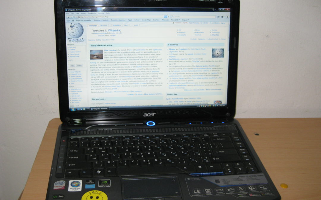 An Acer laptop sits open on a desk. It displays the homepage of Wikipedia.