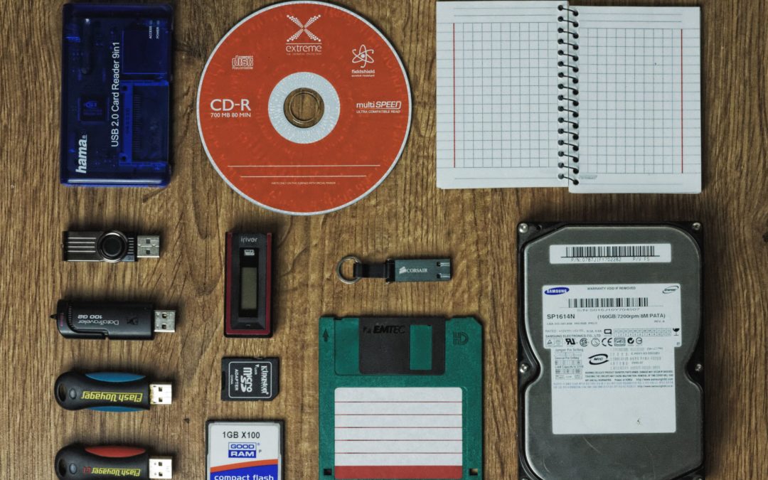 Various forms of data storage media are neatly arranged on a desk. Including USB thumb drives, a CD-R, a hard drive, and various types of memory cards.
