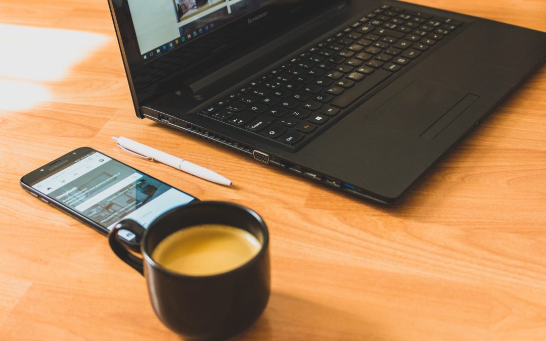 A laptop, mobile phone, and coffee cup are arranged on a wooden tabletop.